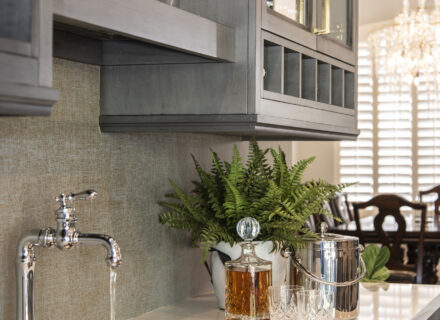 Modern bar lounge with sink, cocktail glasses, ice bucket, and gray cabinets.
