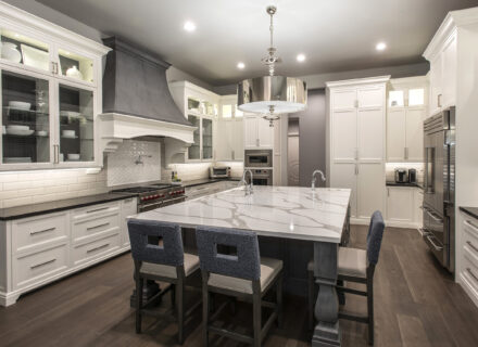 Bright, modern kitchen design with white cabinets and black countertops, marble island, and dark wood floors.