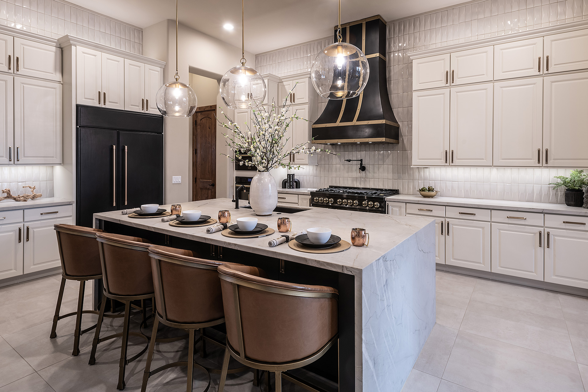 White, spacious kitchen with large island, leather seats, black appliances.