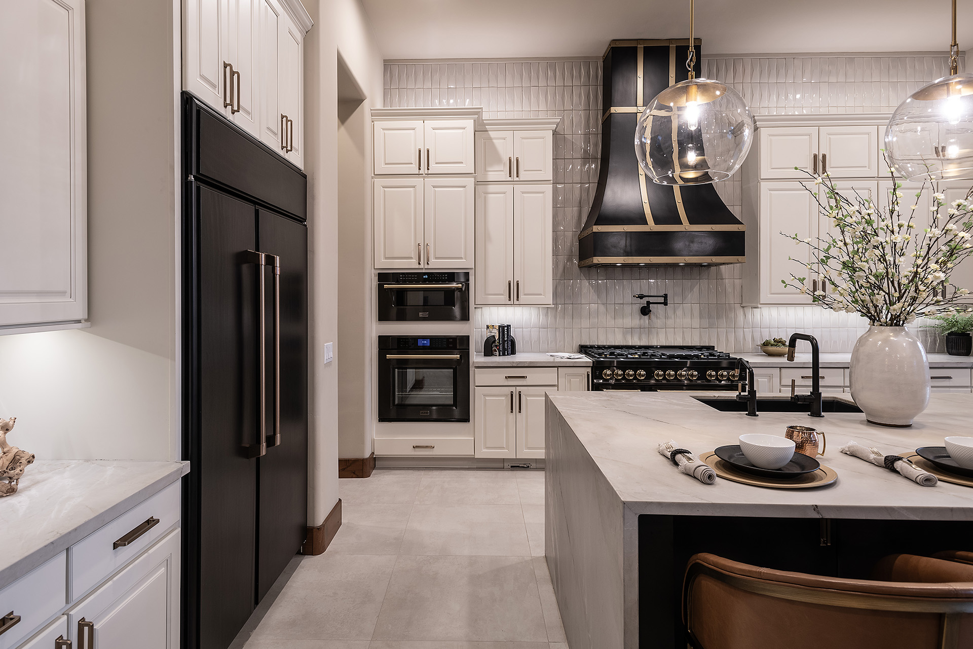 White, spacious kitchen with large island, leather seats, black appliances.